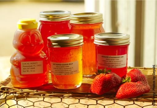 Photo of five jars of honey with a bunch of strawberries on a basket. Left jar is a bee shaped plastic bottle and the others are mason jars. Photo courtesy of Duponi.